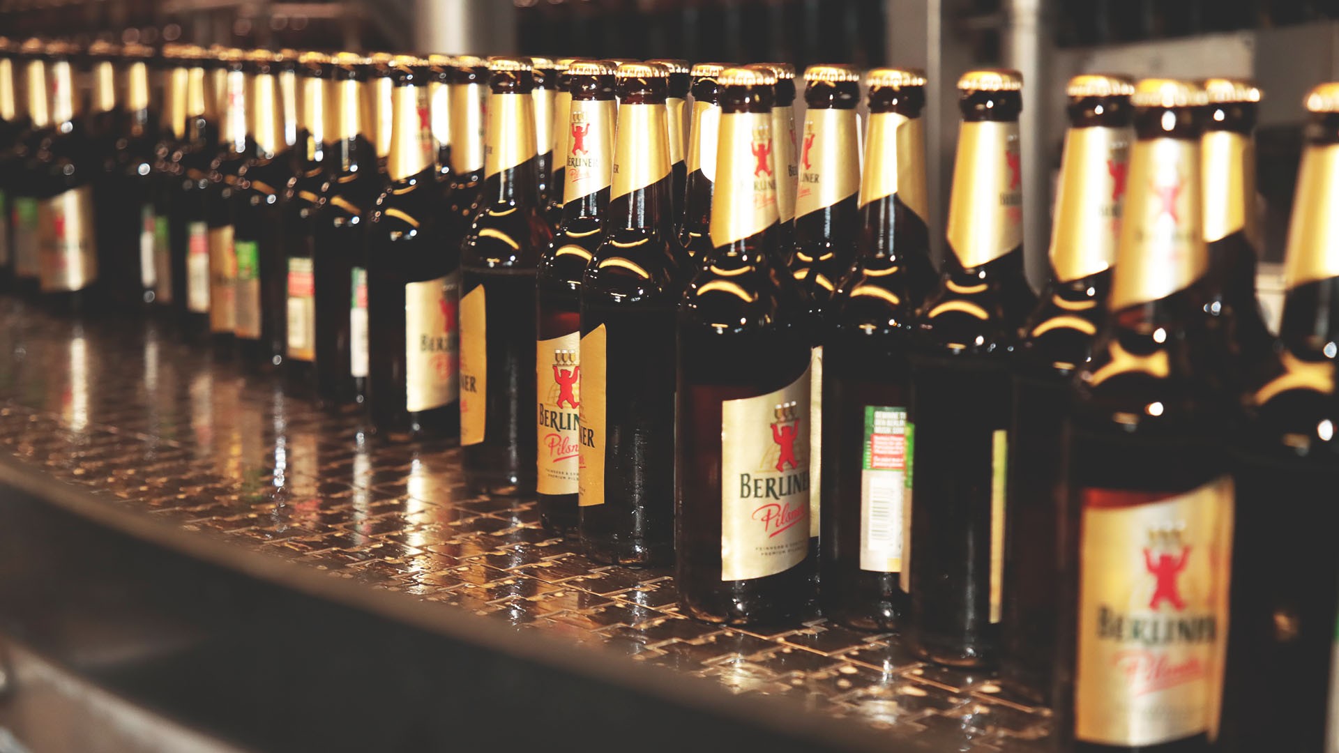 Reihen von Flaschen stehen auf einem Förderband in einer Fabrik. Jede Flasche trägt ein Etikett mit einem roten Wappen.