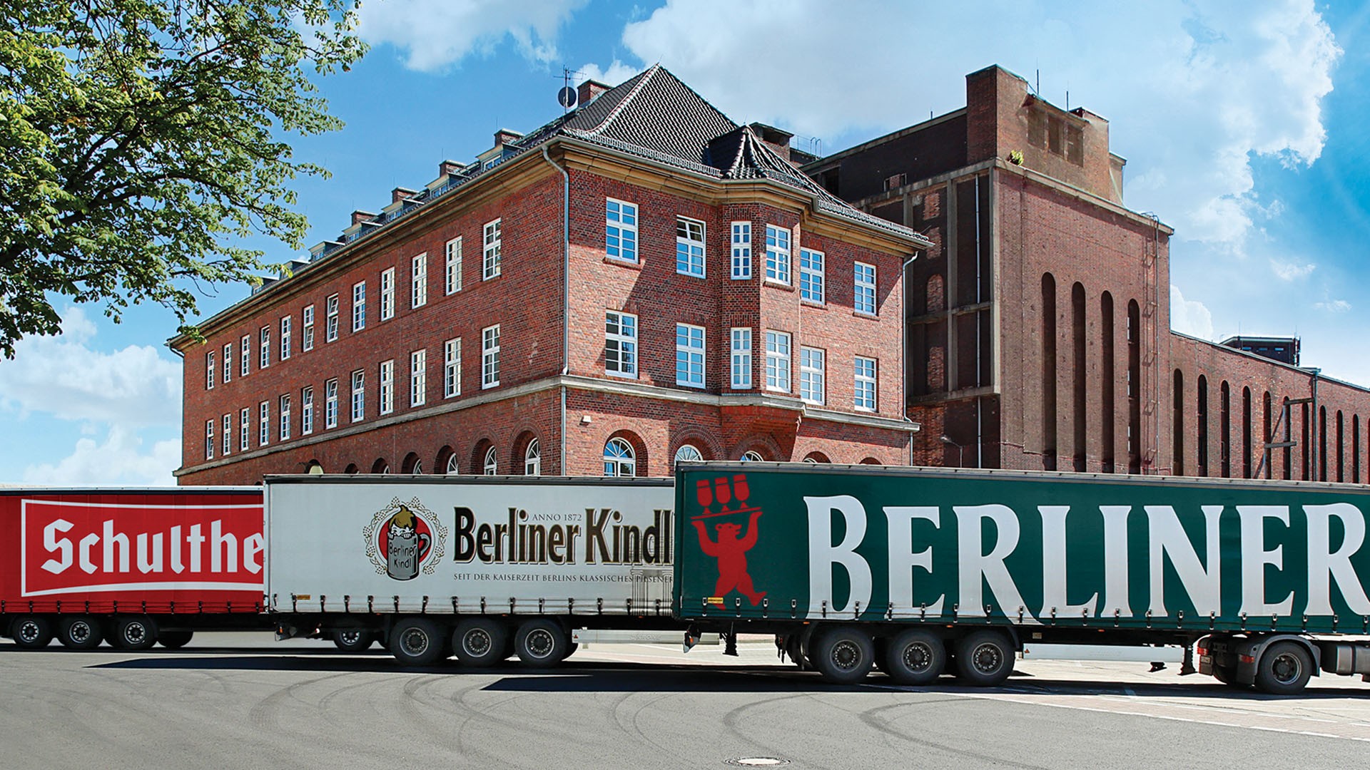 Zwei große Lastwagen fahren an einem roten Backsteingebäude vorbei.
