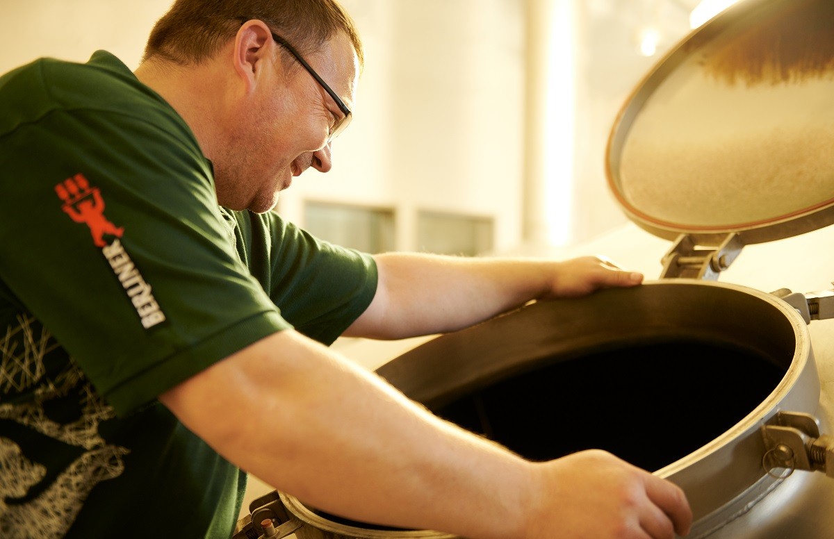 Ein Mann in grünem T-Shirt blickt in einen großen Metallbehälter.