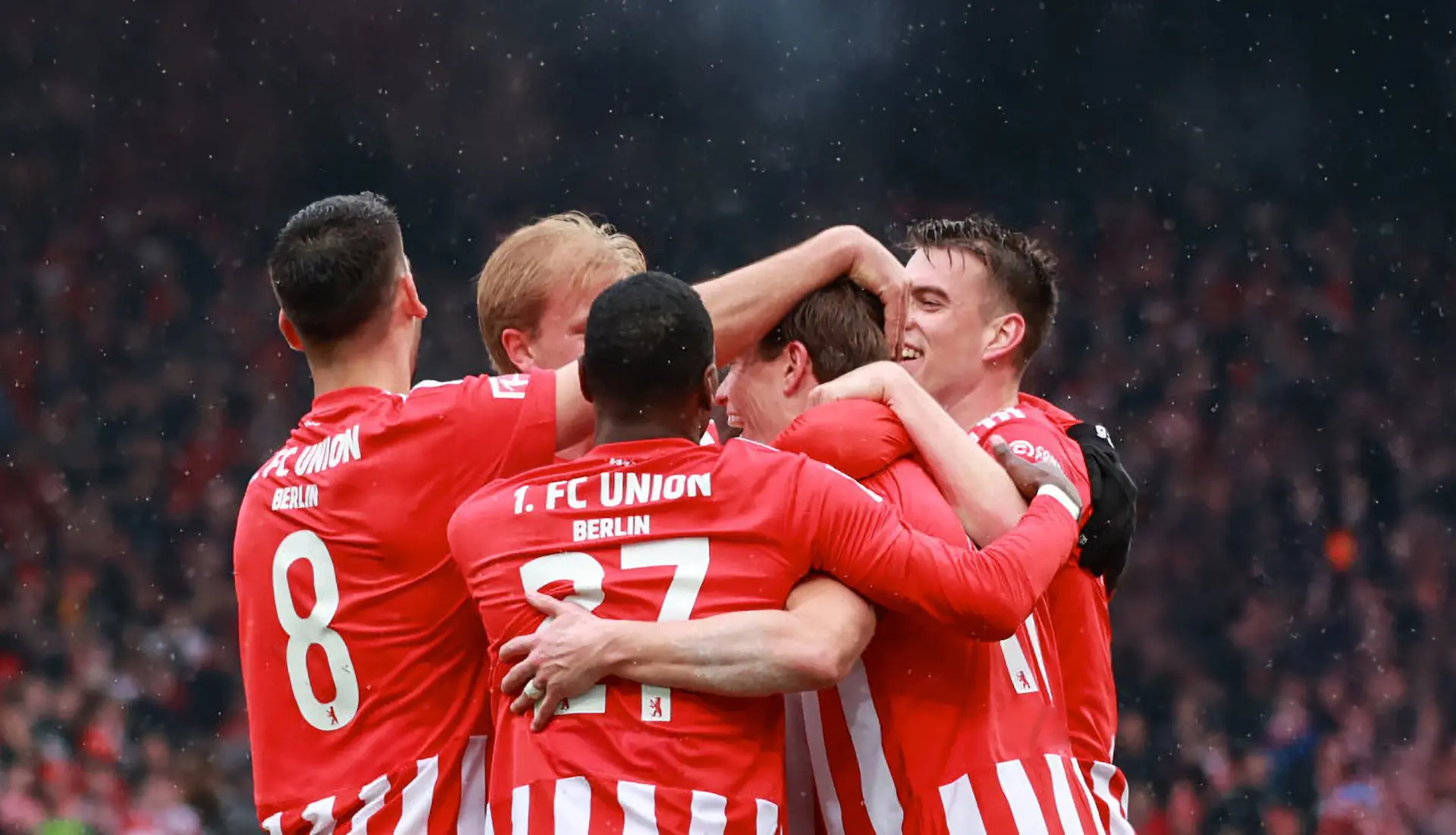 Fünf Fußballspieler von Union Berlin umarmen sich auf dem Spielfeld und feiern ein geschossenes Tor.