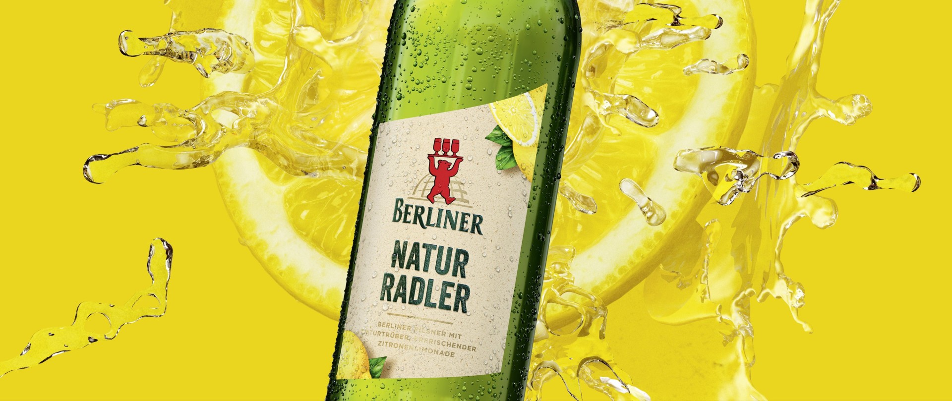 Grüne betaute Bierflasche mit beigem Etikett vor gelben Hintergrund mit eine Zitrone