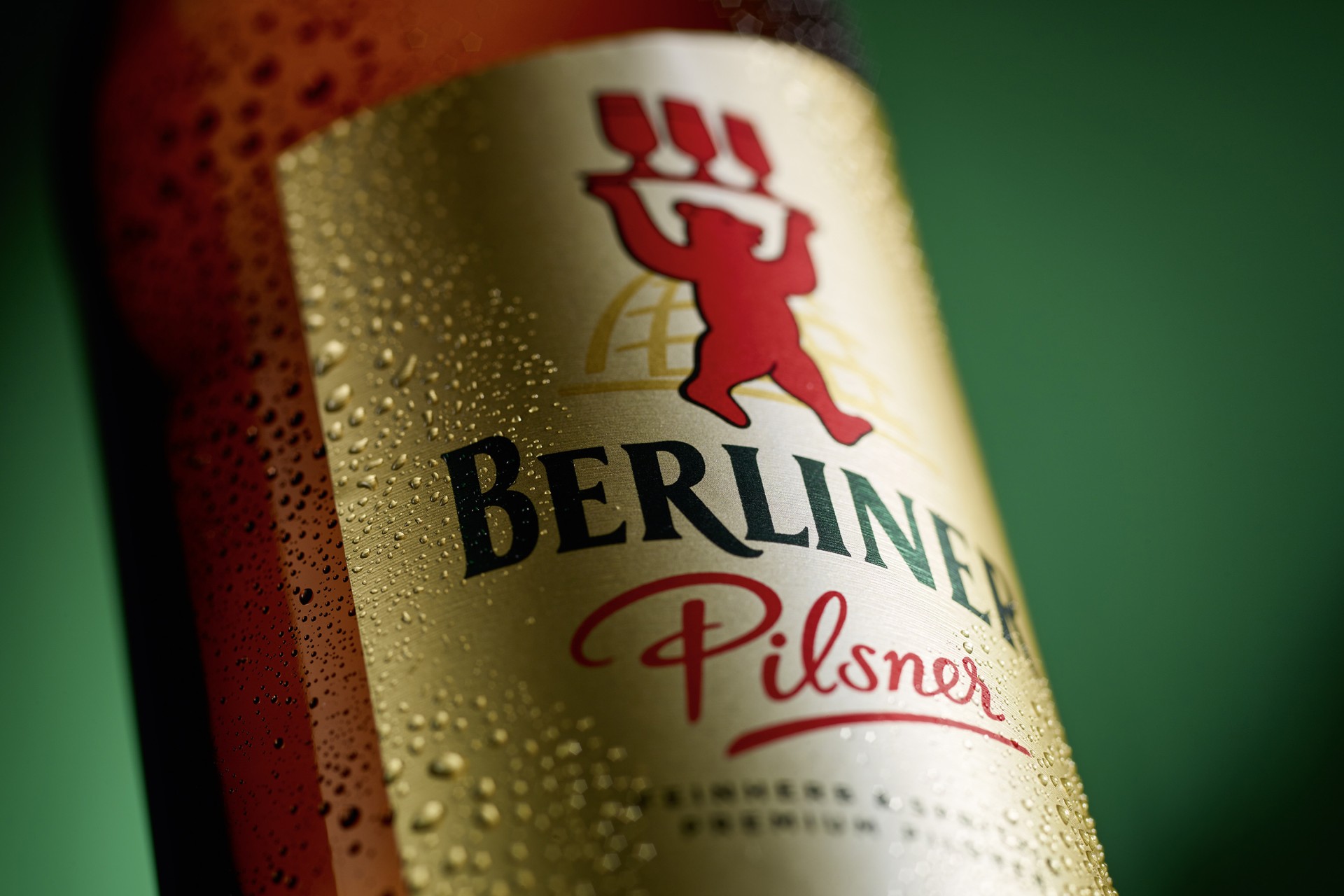 Ausschnitt einer braunen betauten Bierflasche mit goldenem Etikett von Berliner Pilsner vor grünem Hintergrund