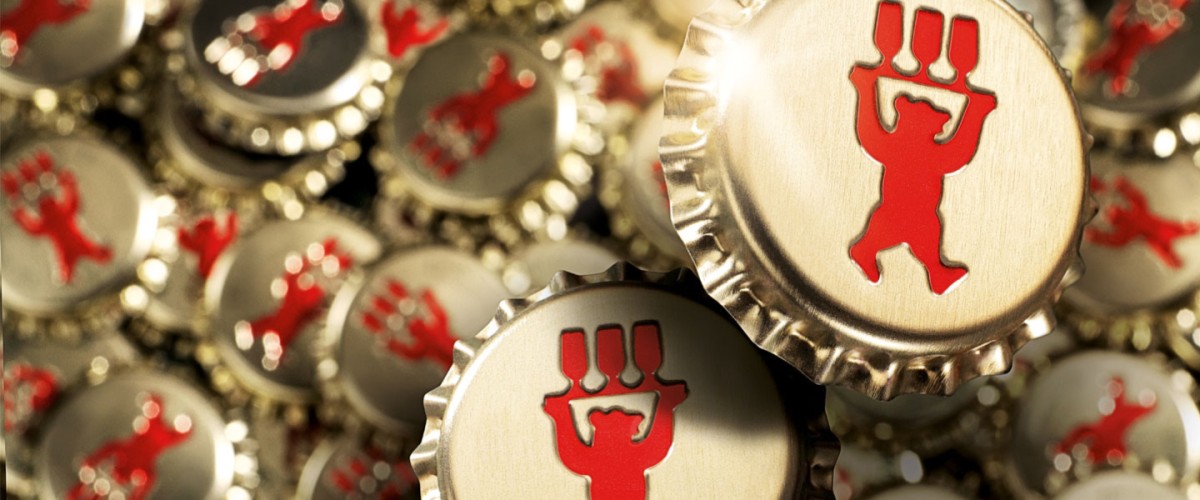 Mehrere Kronkorken sind eng beieinander angeordnet, einige im Fokus, andere unscharf. Jeder Deckel trägt ein rotes Symbol in Form einer tanzenden Figur.