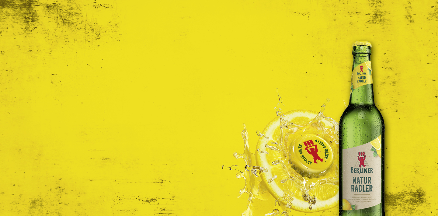 Flasche Berliner Radler vor gelbem Hintergrund. Daneben eine aufge-schnittene Zitrone mit einem gelben Kronkorken als Zentrum.